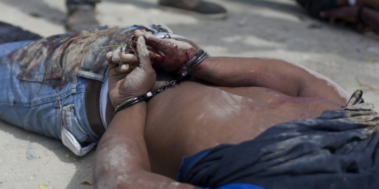 A man's body with his bloodied hands handcuffed lays at a crime scene in Tabarre, a town on the outskirts of Port-au-Prince, Haiti, early Friday, May 1, 2015. Investigators removed three bodies, found handcuffed and blindfolded, from a car that was parked on the side of a street surrounded by open land, and about three blocks from the U.S. embassy. According to police investigators on the scene, the people found dead are Gerda Julien, her brother Robernard Julien and Carl Eduard Guerrier. (AP Photo/Dieu Nalio Chery)