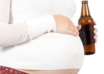 Young pregnant woman holding bottle of beer. Isolated over white