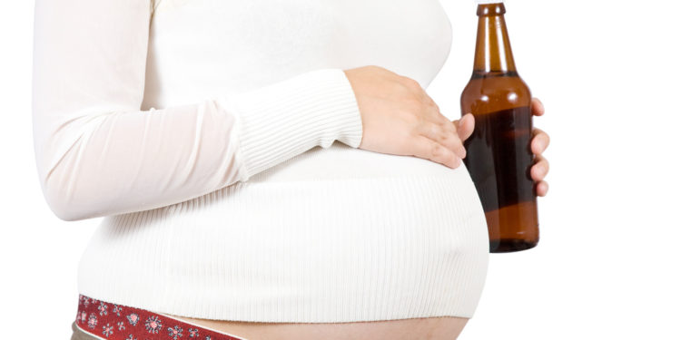 Young pregnant woman holding bottle of beer. Isolated over white