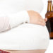 Young pregnant woman holding bottle of beer. Isolated over white