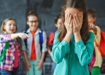 Schoolgirl crying on background of classmates teasing her