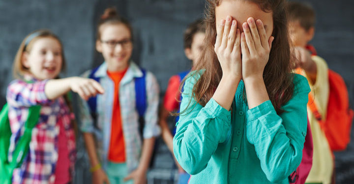 Schoolgirl crying on background of classmates teasing her