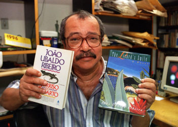 O escritor João Ubaldo Ribeiro com seu livro "O Sorriso do Lagarto", as edições brasileira e em língua inglesa. (Sem local, 26.01.1996. Foto de André Durão/Folhapress)