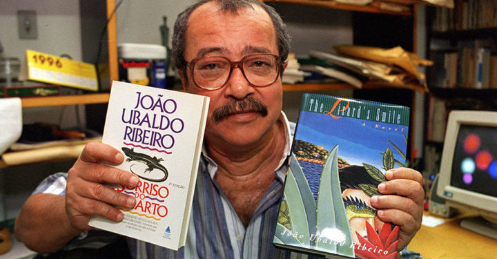 O escritor João Ubaldo Ribeiro com seu livro "O Sorriso do Lagarto", as edições brasileira e em língua inglesa. (Sem local, 26.01.1996. Foto de André Durão/Folhapress)