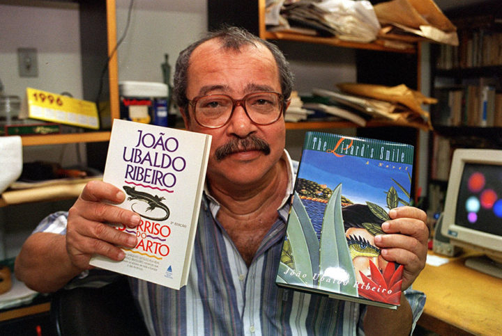 O escritor João Ubaldo Ribeiro com seu livro "O Sorriso do Lagarto", as edições brasileira e em língua inglesa. (Sem local, 26.01.1996. Foto de André Durão/Folhapress)