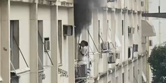Mulher se abriga na área externa de prédio após incêndio atingir apartamento em Copacabana, na Zona Sul do Rio.